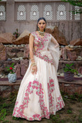 Woman in a white and pink embroidered dress standing in front of a stone wall with decorative elements.